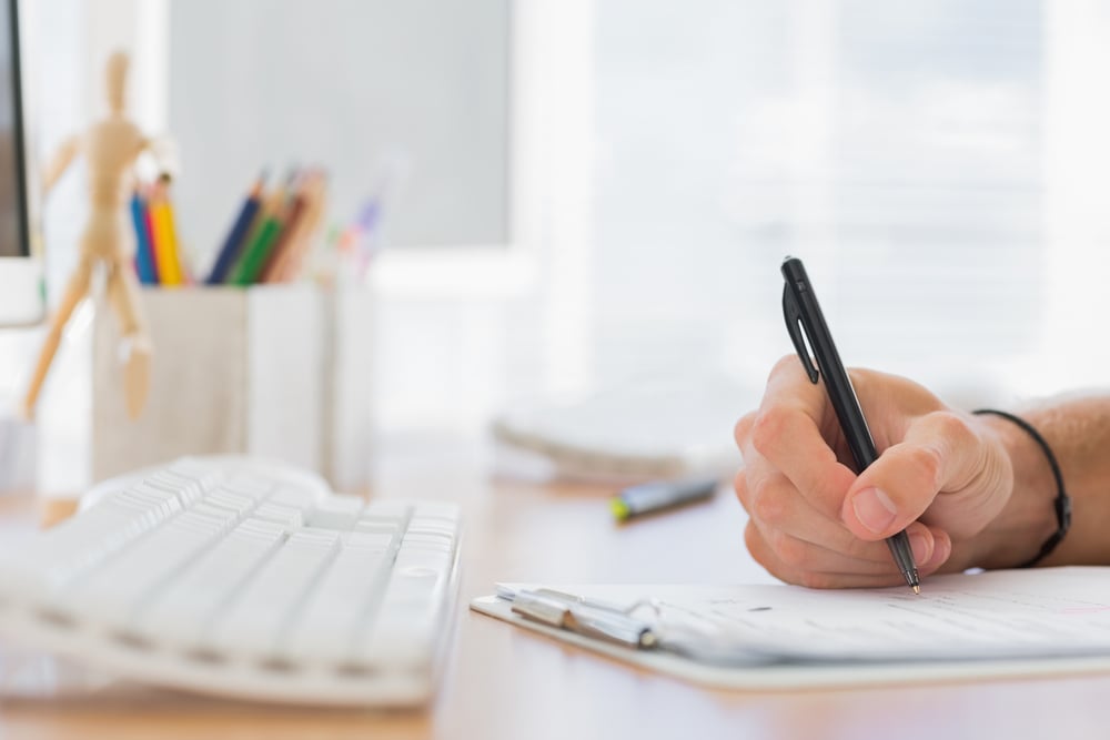 Close up of a hand writing in a modern office on a clipboard Close up of a hand writing in a modern office on a clipboard