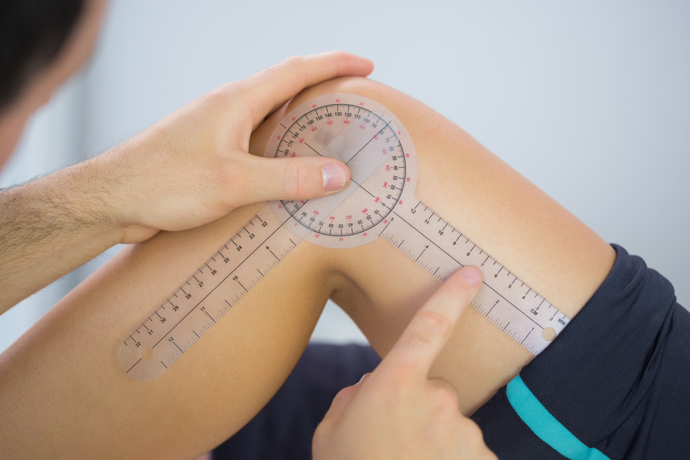 Physiotherapist examining knee angle with goniometer in bright office Physiotherapist examining knee angle with goniometer in bright office